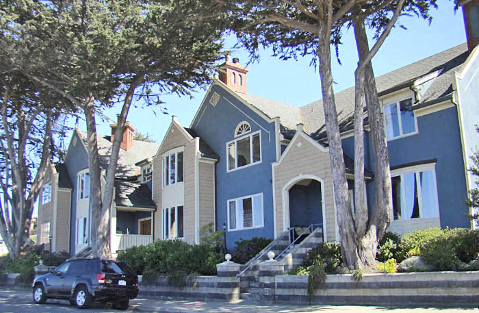 A black car is parked on the street in front of a blue house.